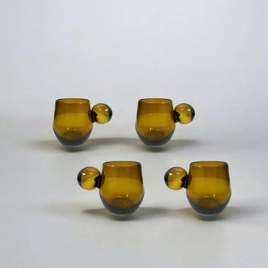 Four amber glass tumblers with black bases on a white background