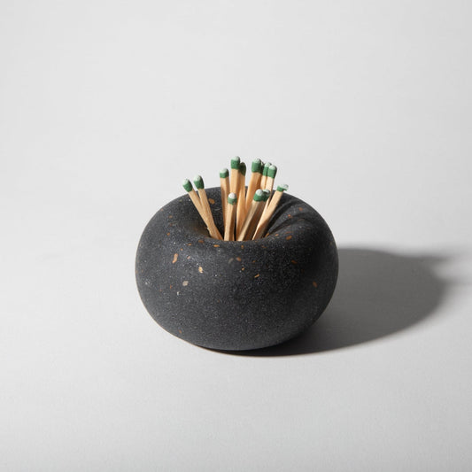 Black ceramic match holder with matches on a light gray background