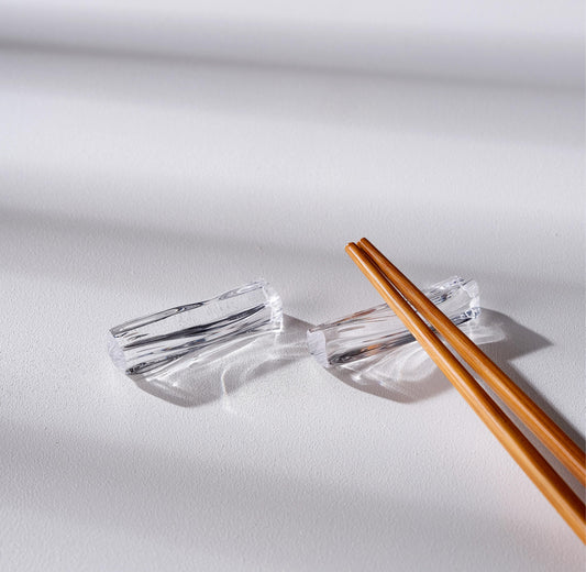 Clear acrylic chopstick rest with wooden chopsticks on a light gray background