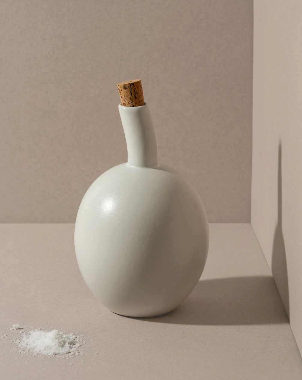 White ceramic bottle with a cork stopper on a beige background
