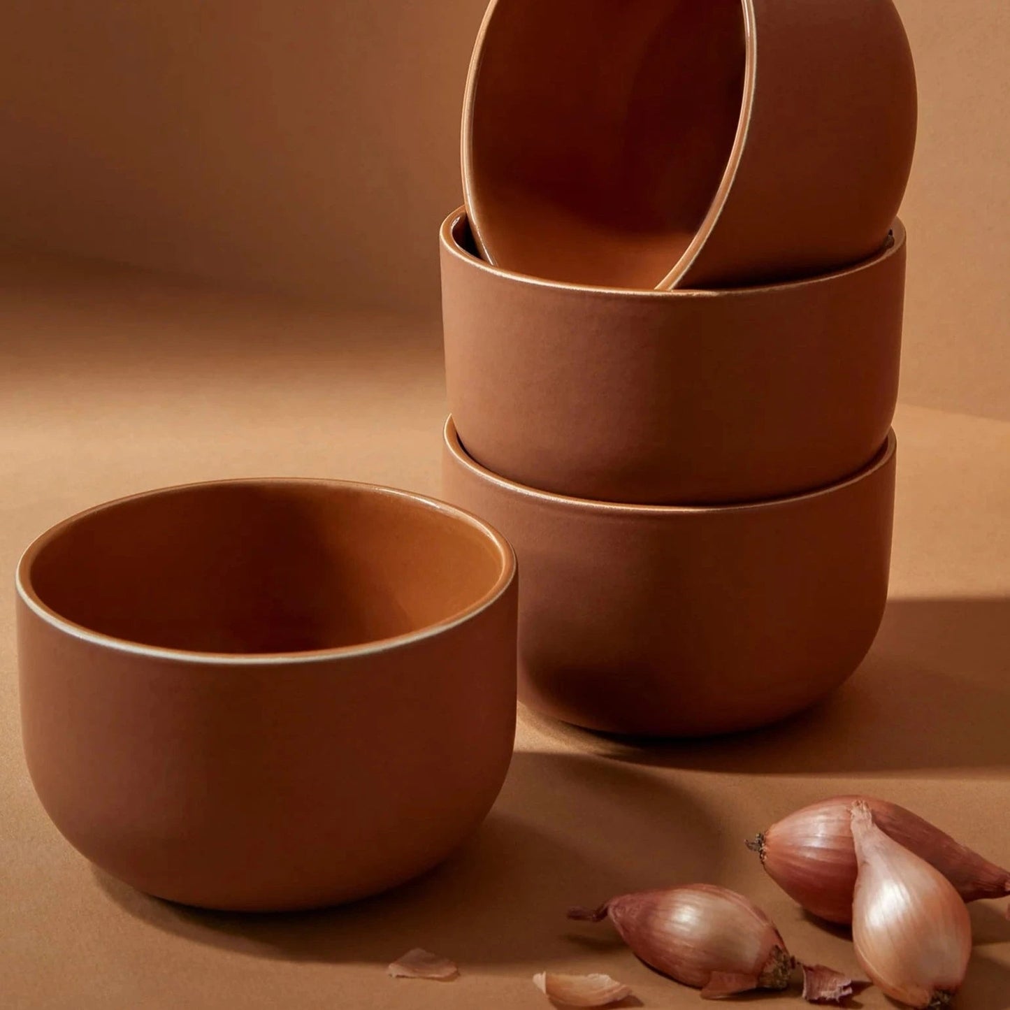 Set of brown ceramic bowls on a brown background with garlic bulbs.