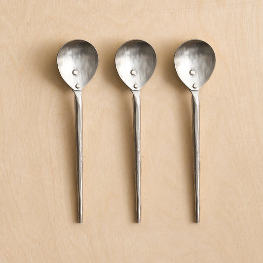 Three silver spoons with textured handles on a beige background
