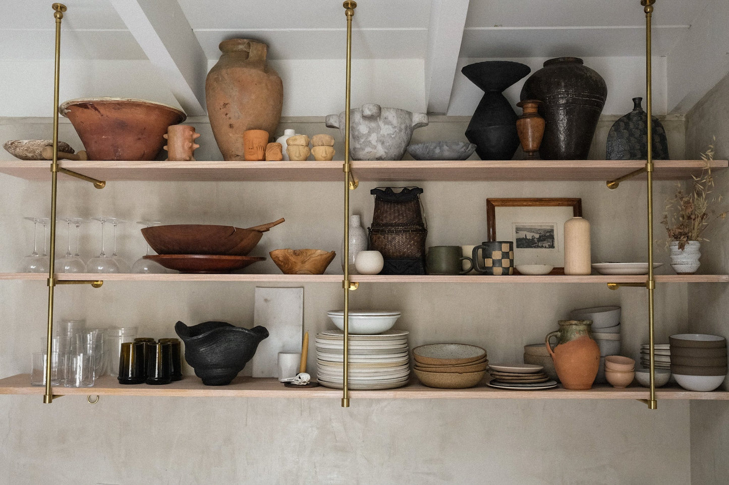 Shelves with various ceramic items in a room with white walls and wooden floor.