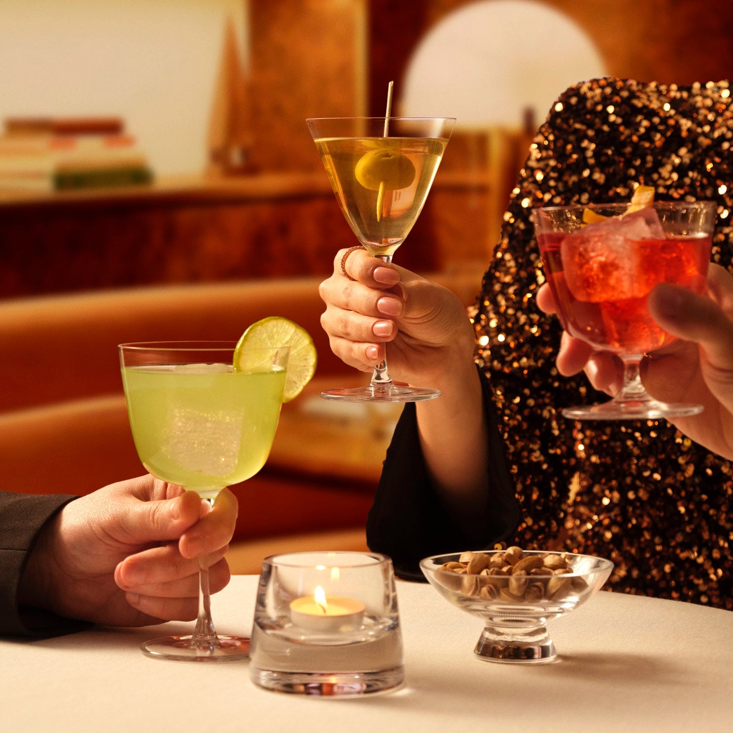 Two people holding cocktails at a table with a warm, intimate setting.