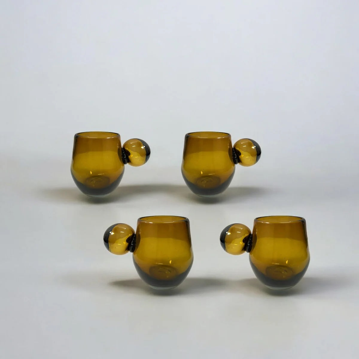 Four amber glass tumblers with black bases on a white background