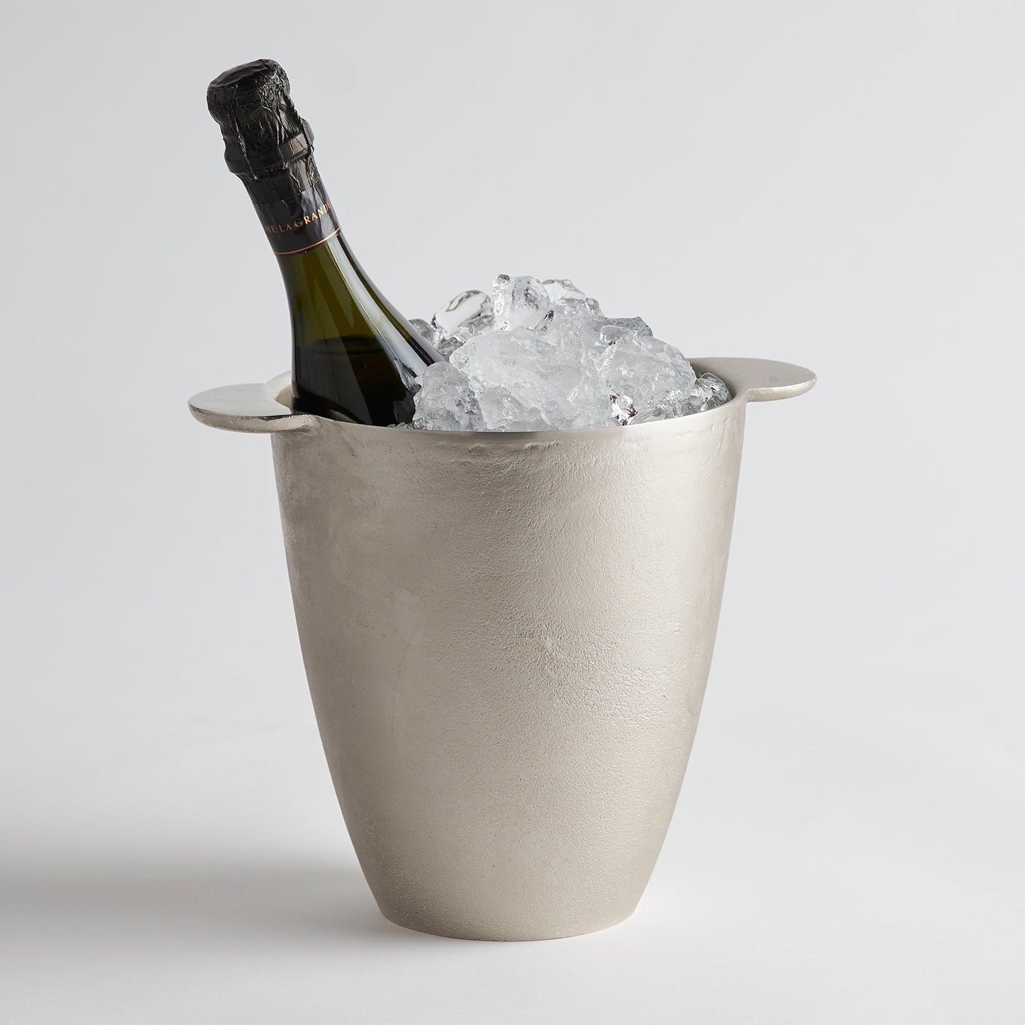 Bottle of champagne in a concrete ice bucket with ice cubes on a light gray background