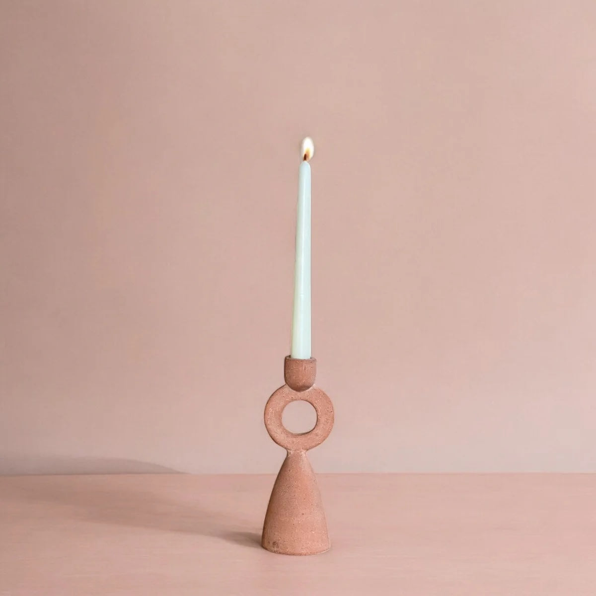 Ceramic candle holder with a lit candle on a beige background