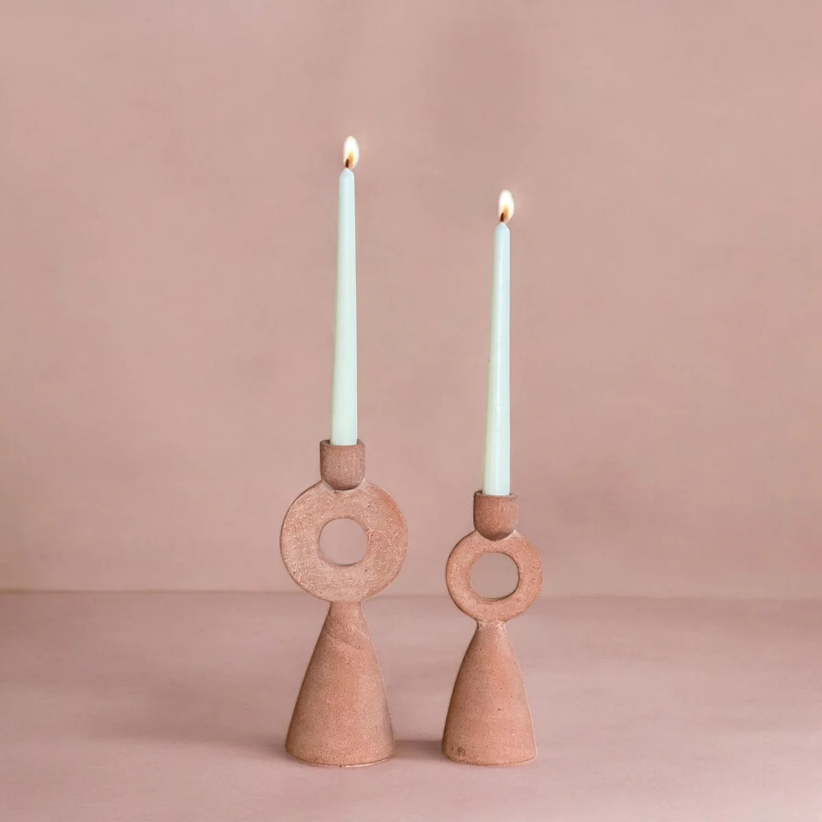 Two terracotta candle holders with lit candles on a pink background