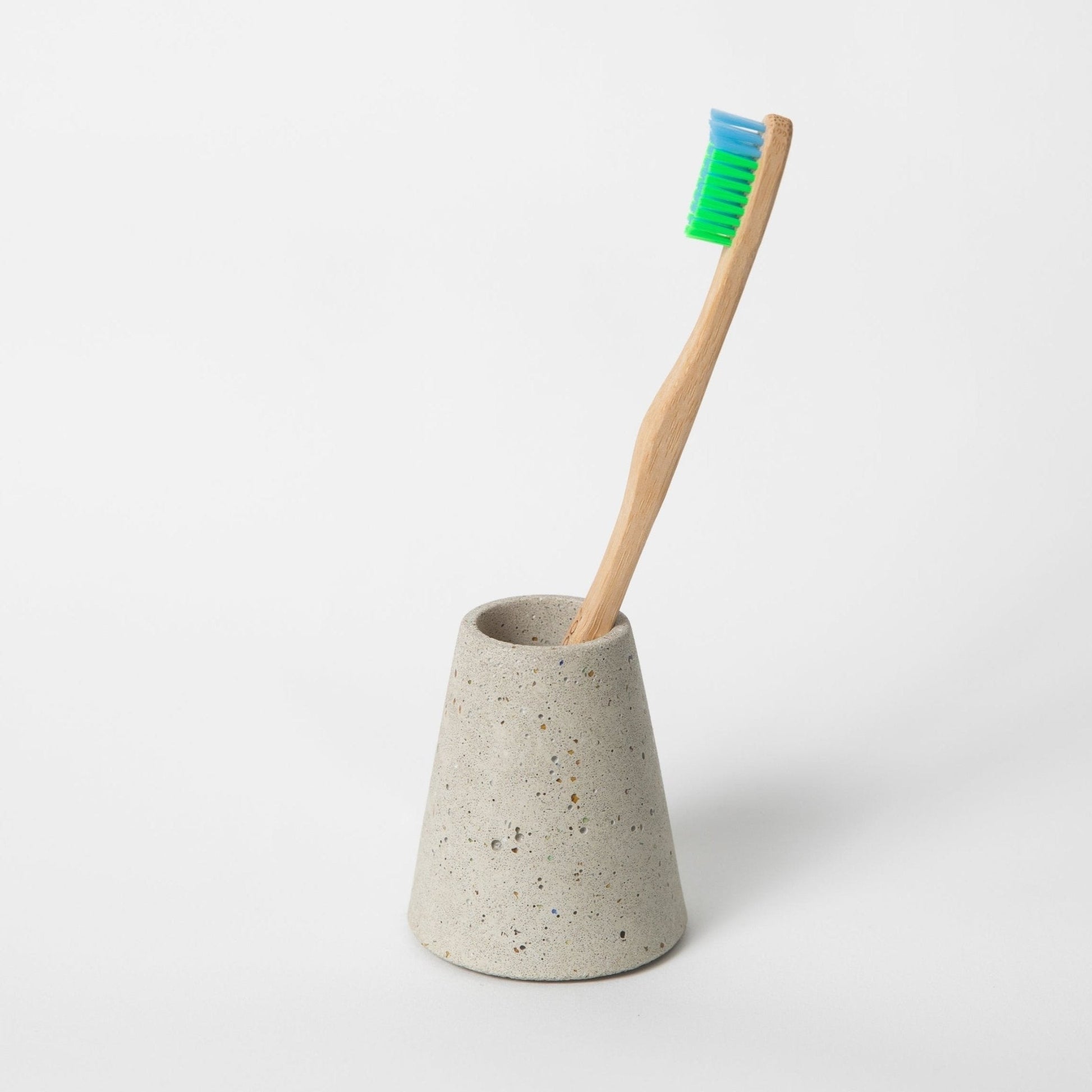 Concrete toothbrush holder with a bamboo toothbrush on a white background