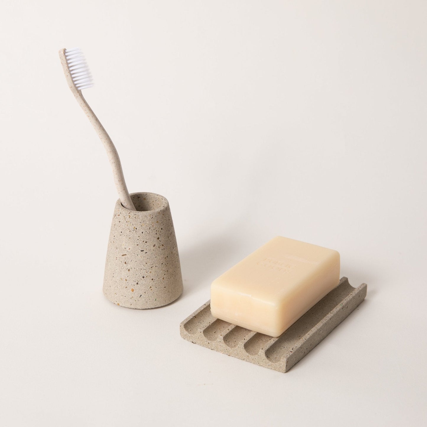 Concrete toothbrush holder with a toothbrush and soap on a concrete soap dish on a light background