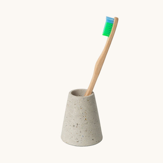 Concrete toothbrush holder with a bamboo toothbrush on a white background
