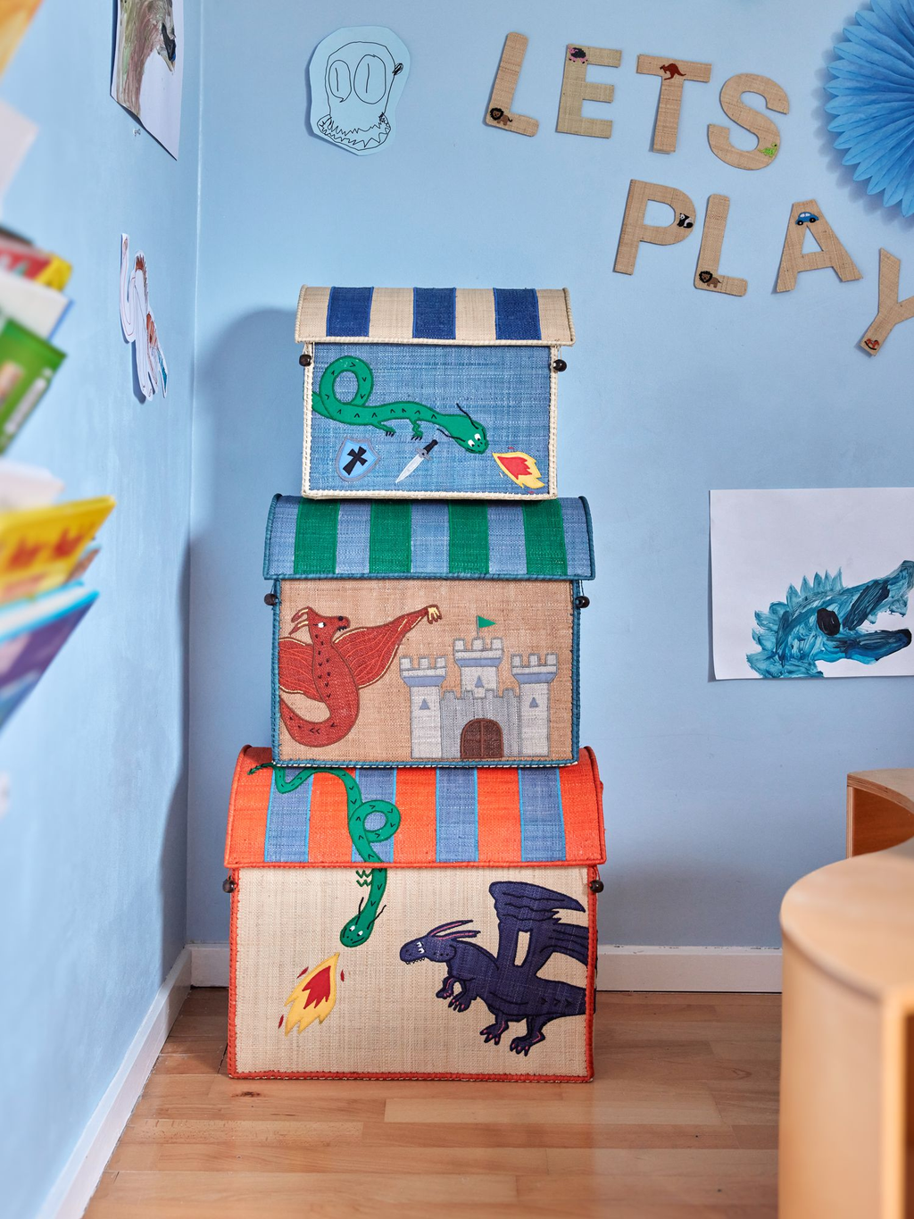 Stack of colorful toy boxes with dragon designs on a blue wall with 'Let's Play' sign.