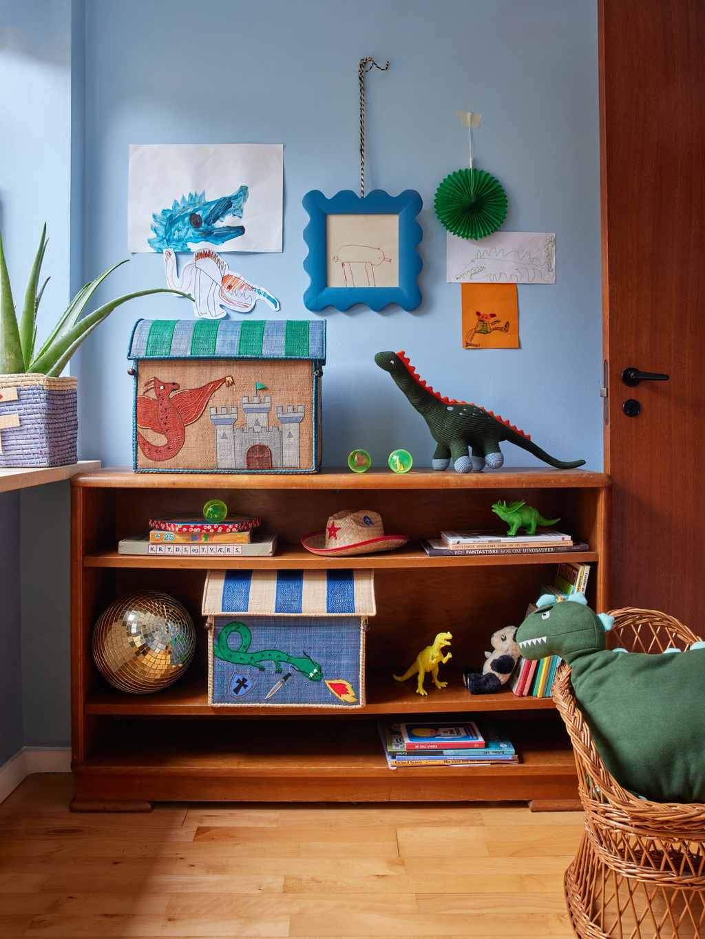Children's room with wooden bookshelf, toys, and decorations against a blue wall.