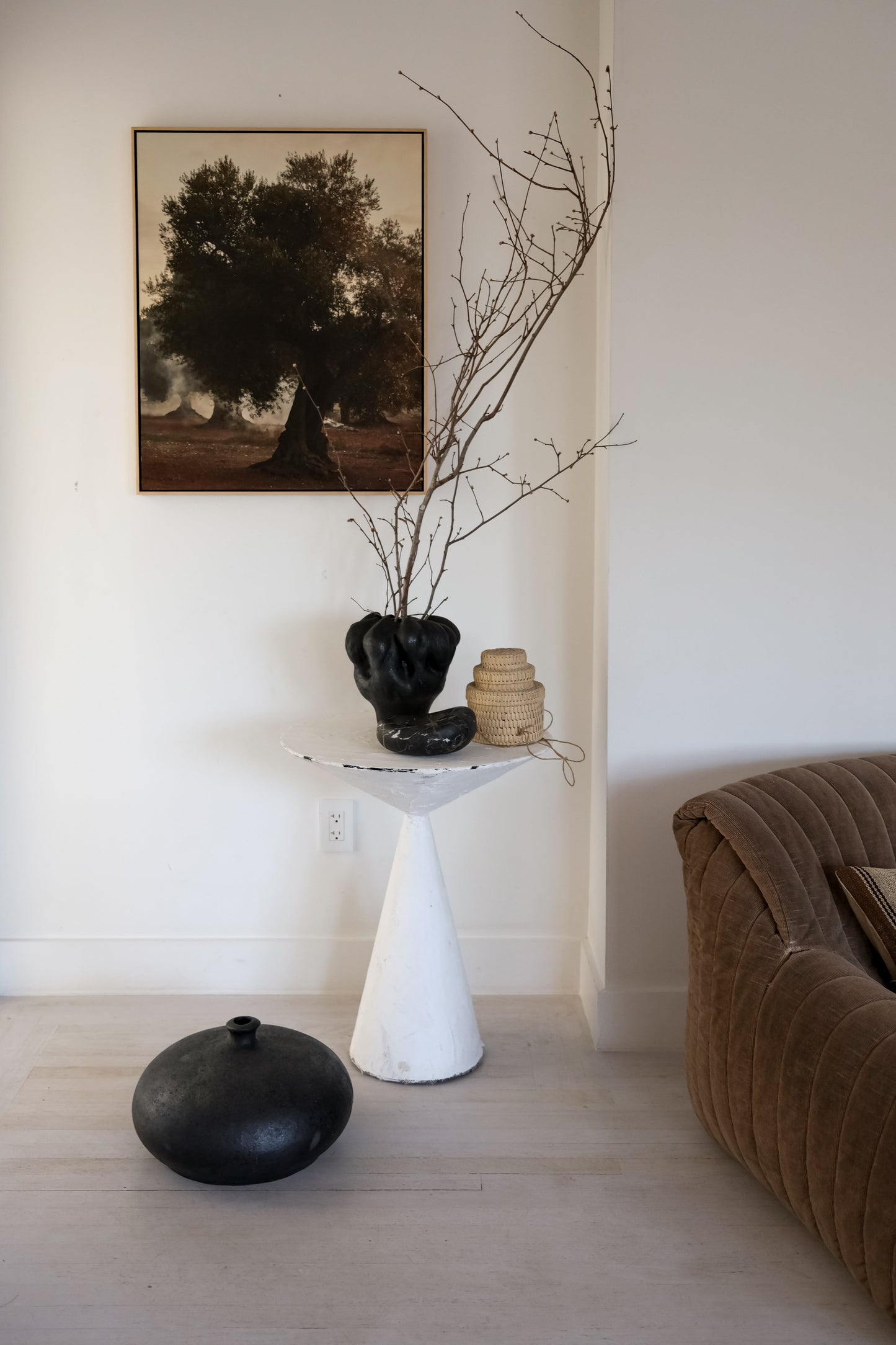 Modern interior with a white pedestal table, black vase, and brown sofa.
