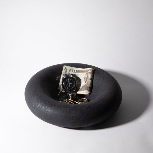 Black dish with a watch, keys, and dollar bill on a white background