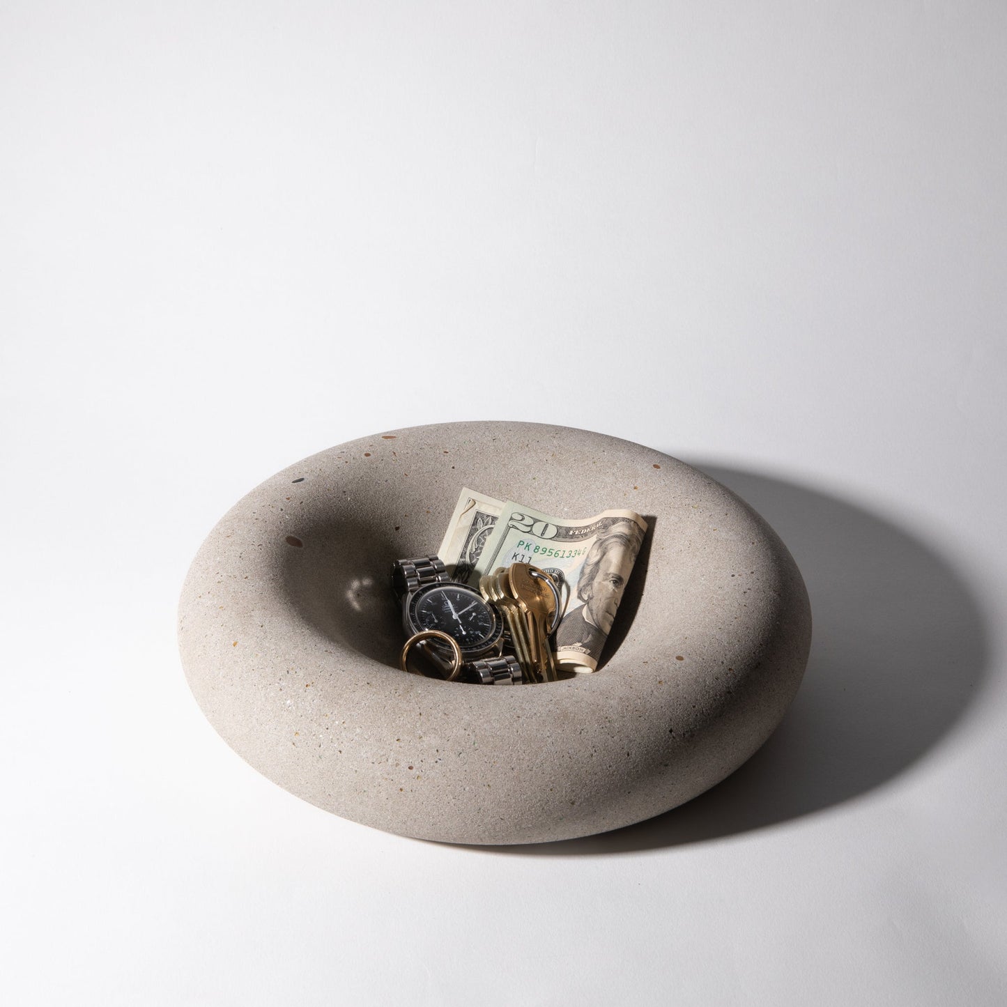 Concrete bowl with money, keys, and a watch on a light gray background