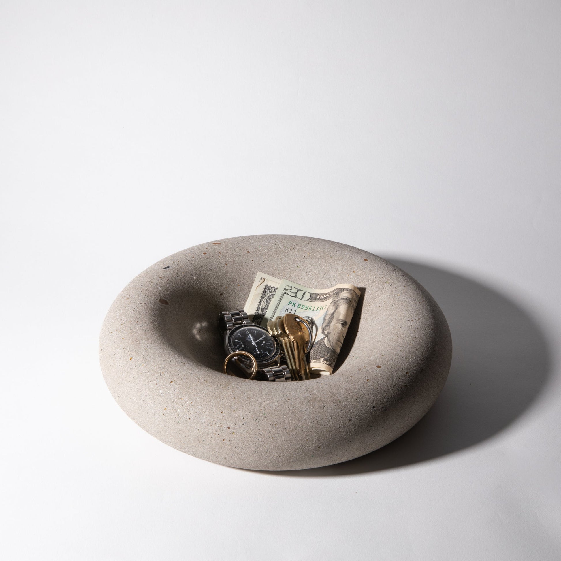 Concrete bowl with money, keys, and a watch on a light gray background
