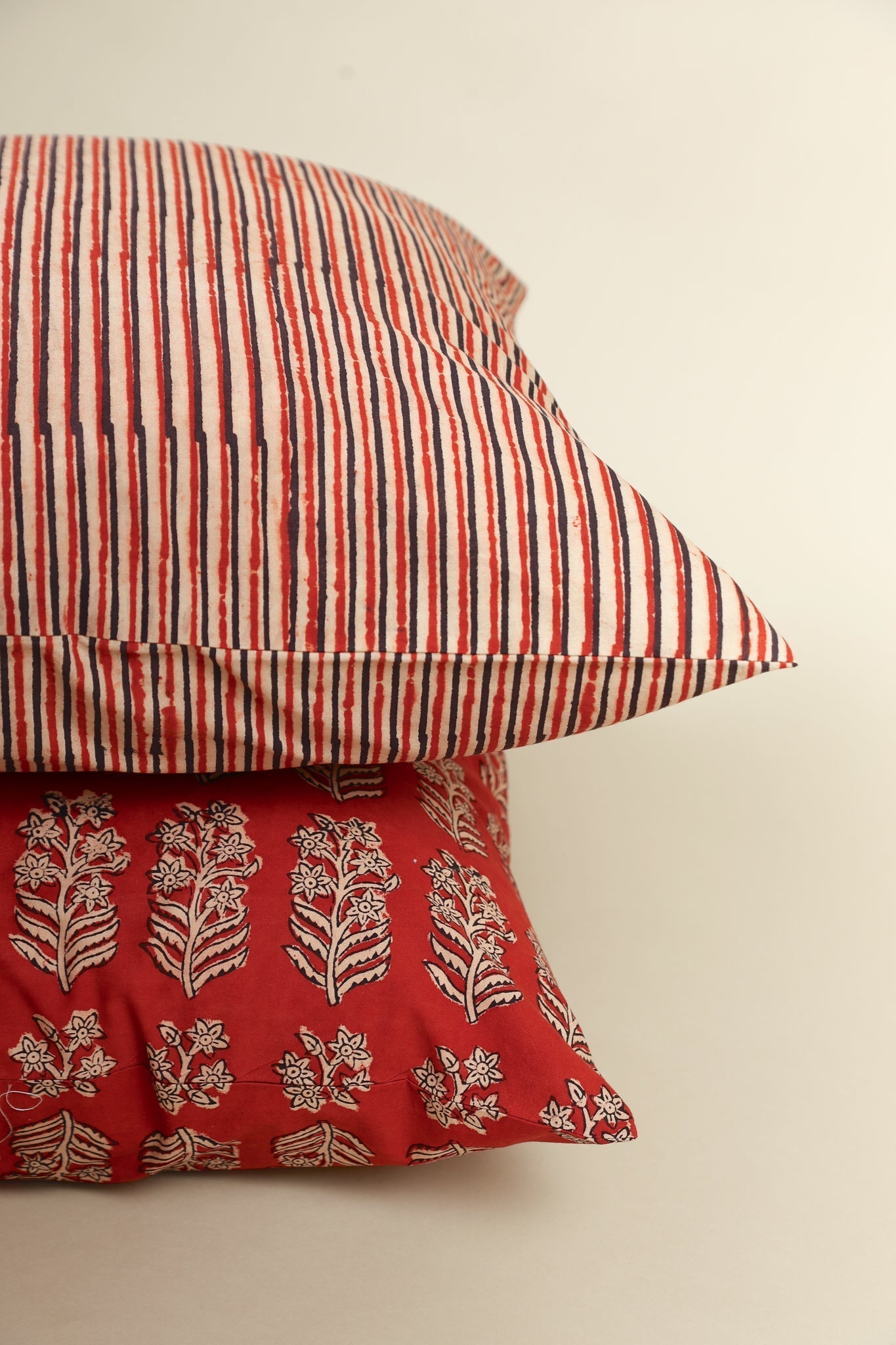 Two pillows, one with red and white stripes and the other with a floral pattern on a beige background