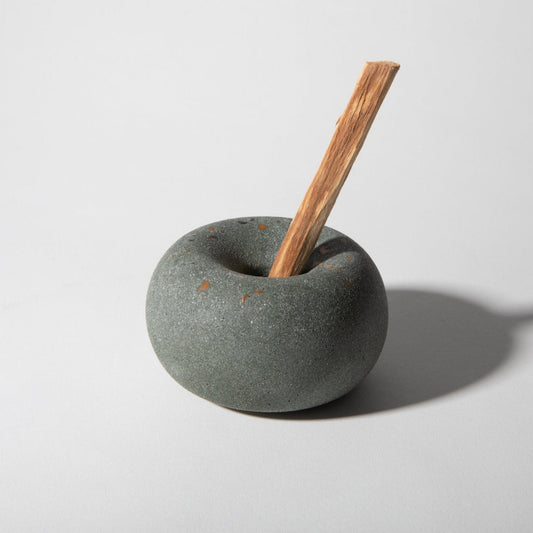 Cylindrical stone holder with a wooden tool on a light gray background