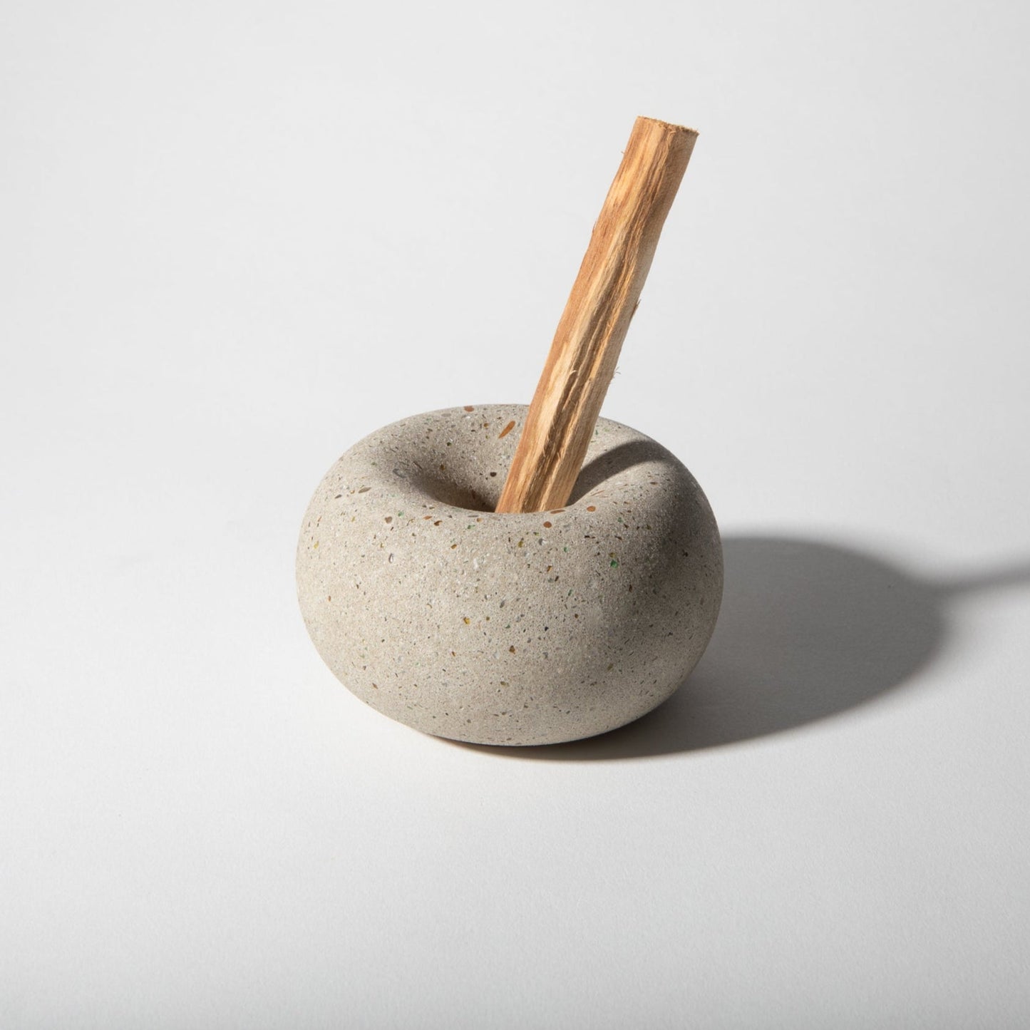 Cylindrical stone container with a wooden stick on a light gray background