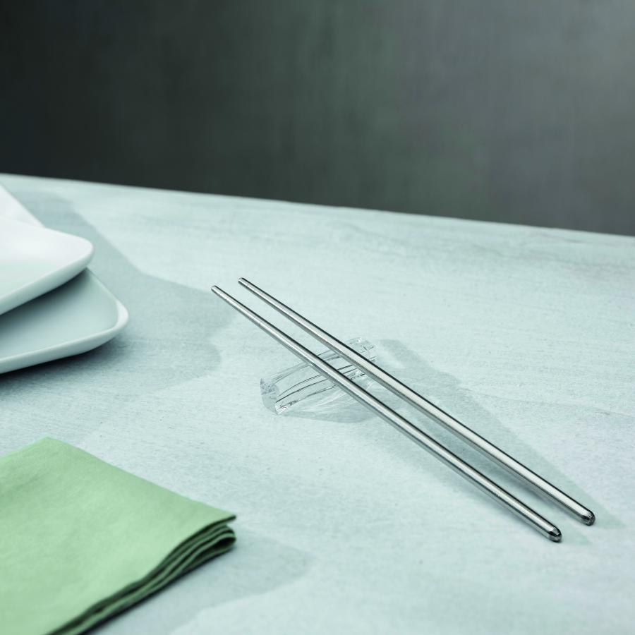 Metallic chopsticks on a light gray surface with a green napkin and white plates in the background.