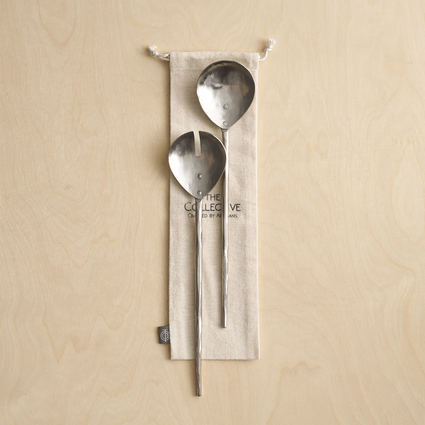 Two metal spoons hanging from a beige fabric pouch on a beige background