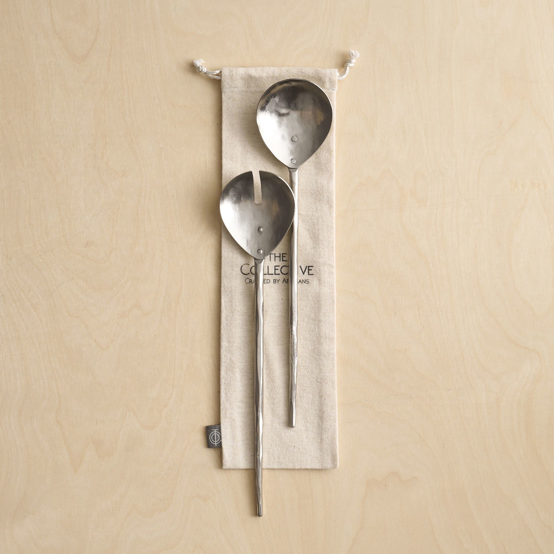 Two metal spoons hanging from a beige fabric pouch on a beige background