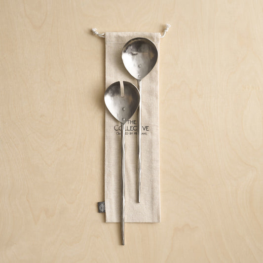 Two metal spoons hanging from a beige fabric pouch on a beige background