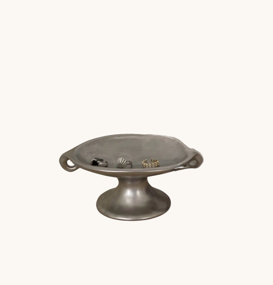 Metallic pedestal dish with shell designs on a white background