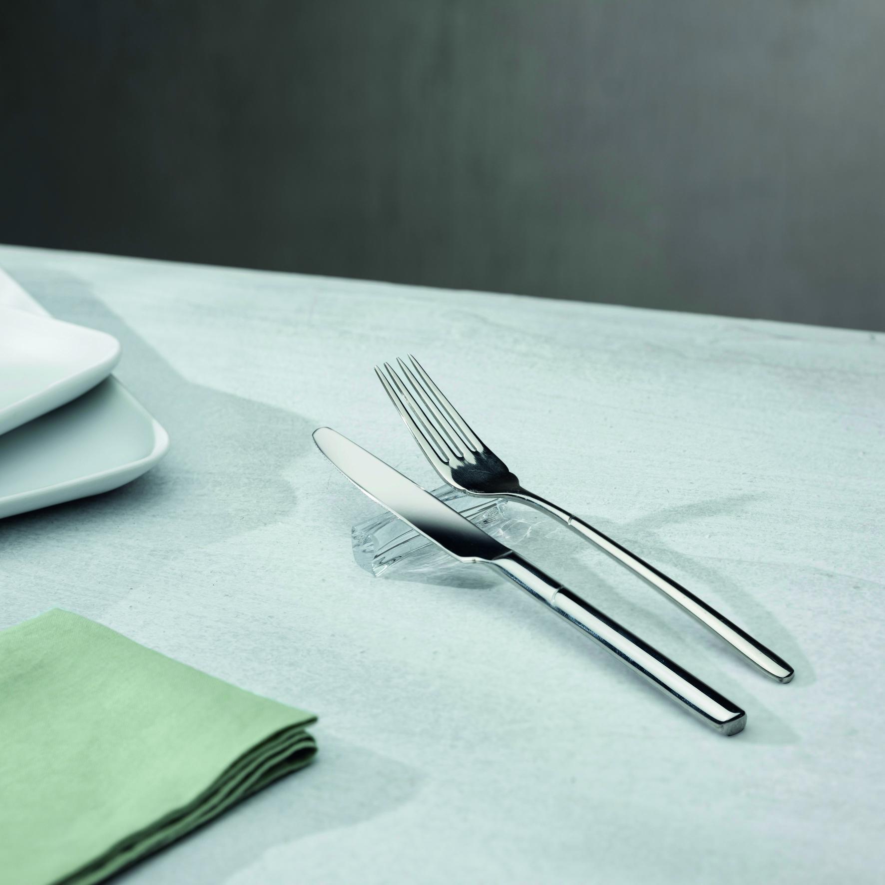 Silver knife and fork on a light blue tablecloth with a green napkin.