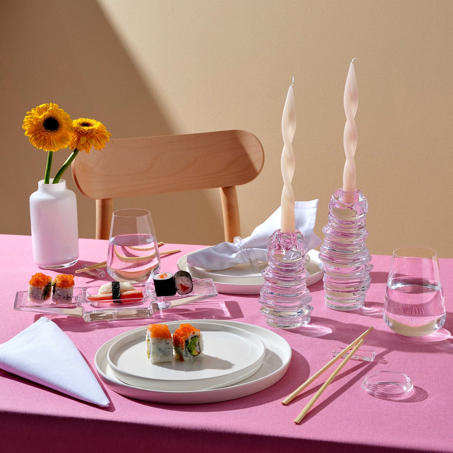 Table setting with sushi, flowers, and candles on a pink tablecloth.