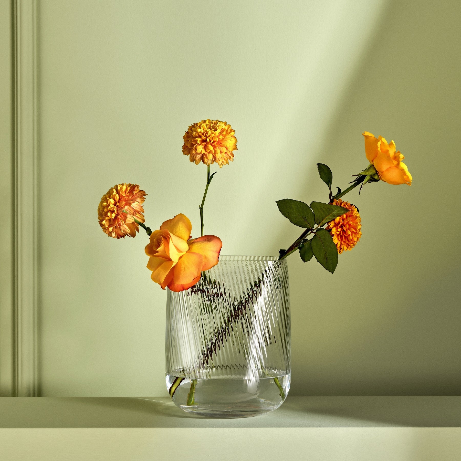 Clear glass vase with orange flowers on a light green background