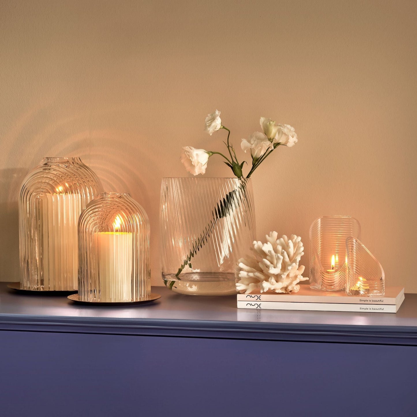 Decorative setup with glass vases, candles, and a vase with flowers on a blue surface.