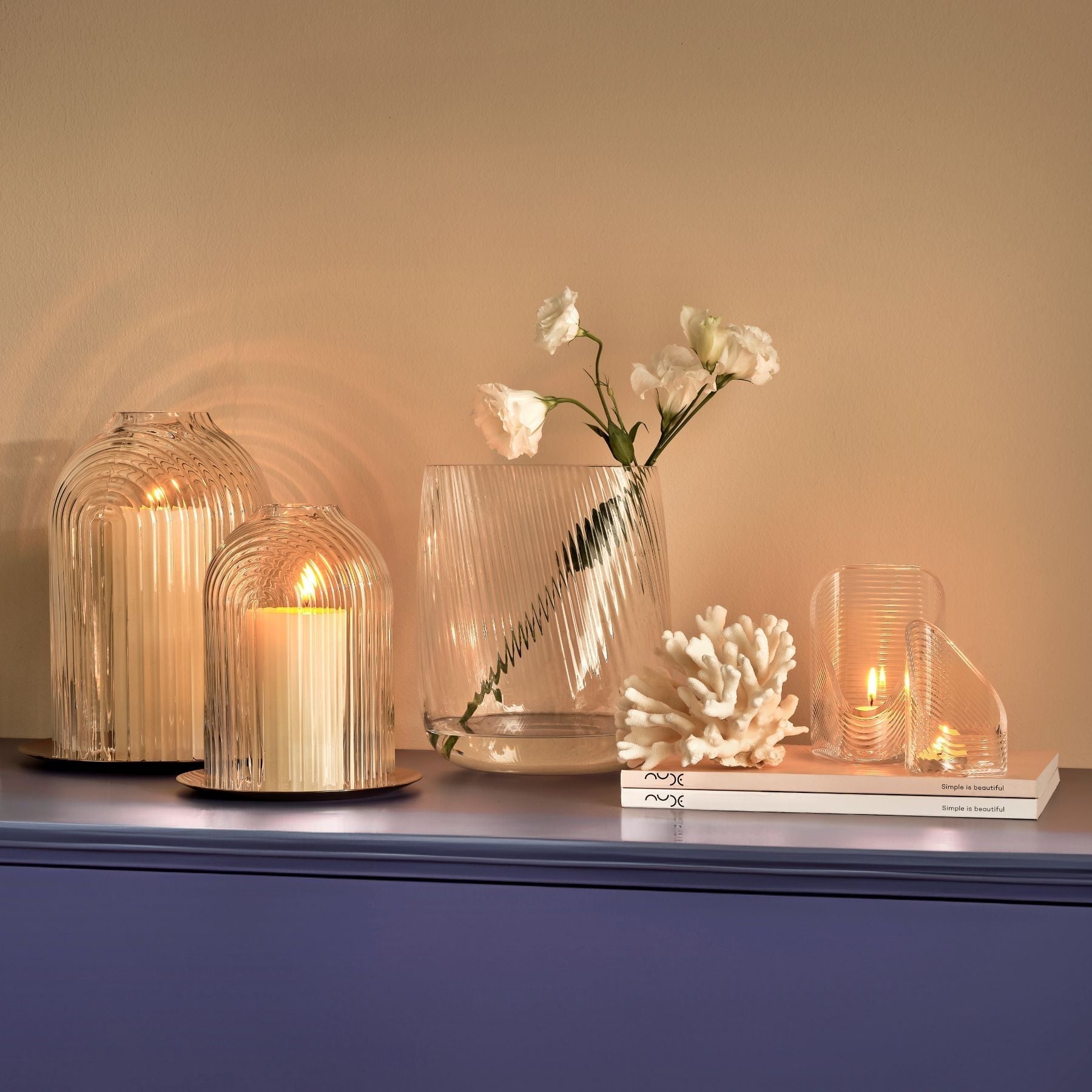 Decorative setup with glass vases, candles, and a vase with flowers on a blue surface.