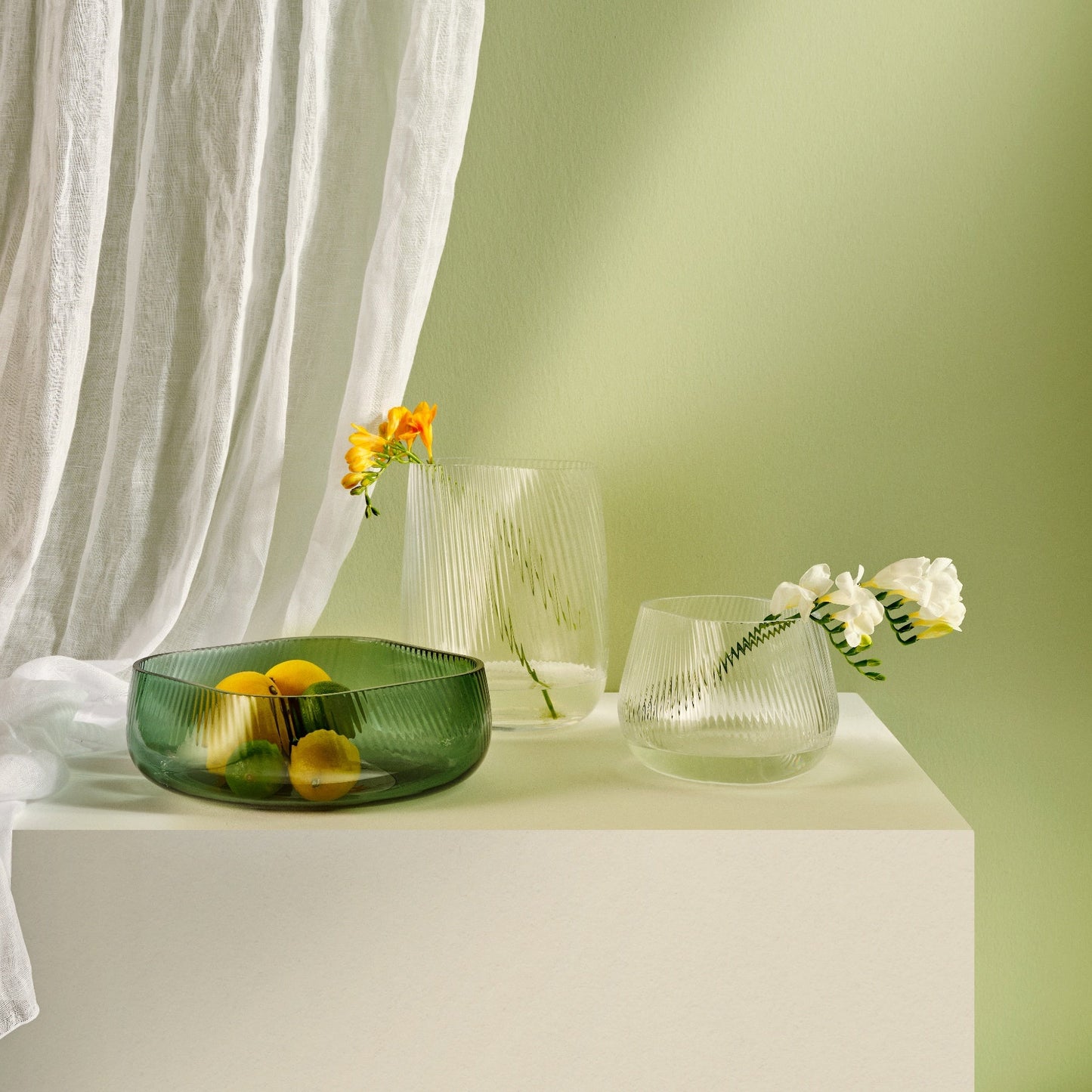 Decorative glass bowl and candle holders on a white surface with a light green background