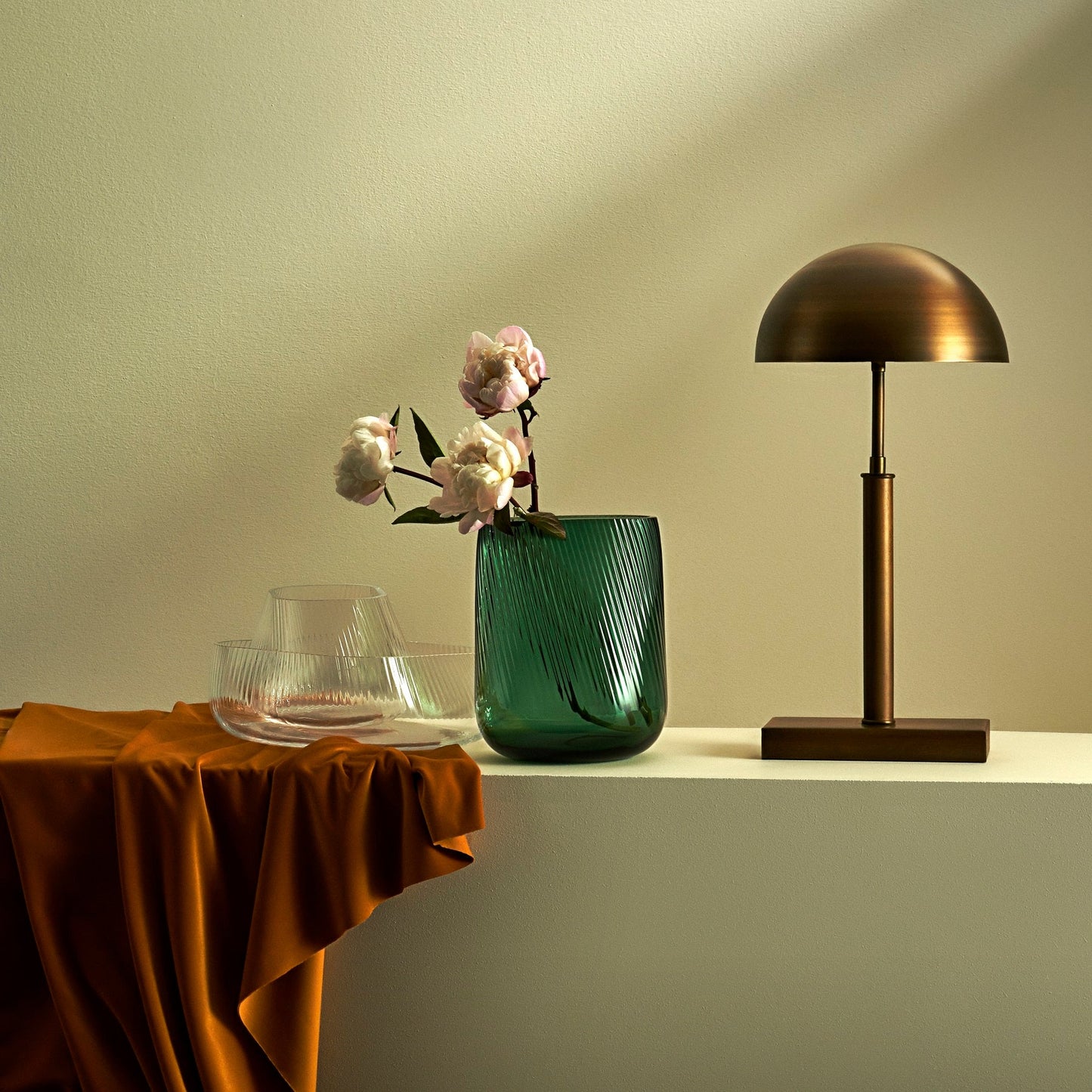 Green vase with flowers and bronze lamp on a table against a beige wall