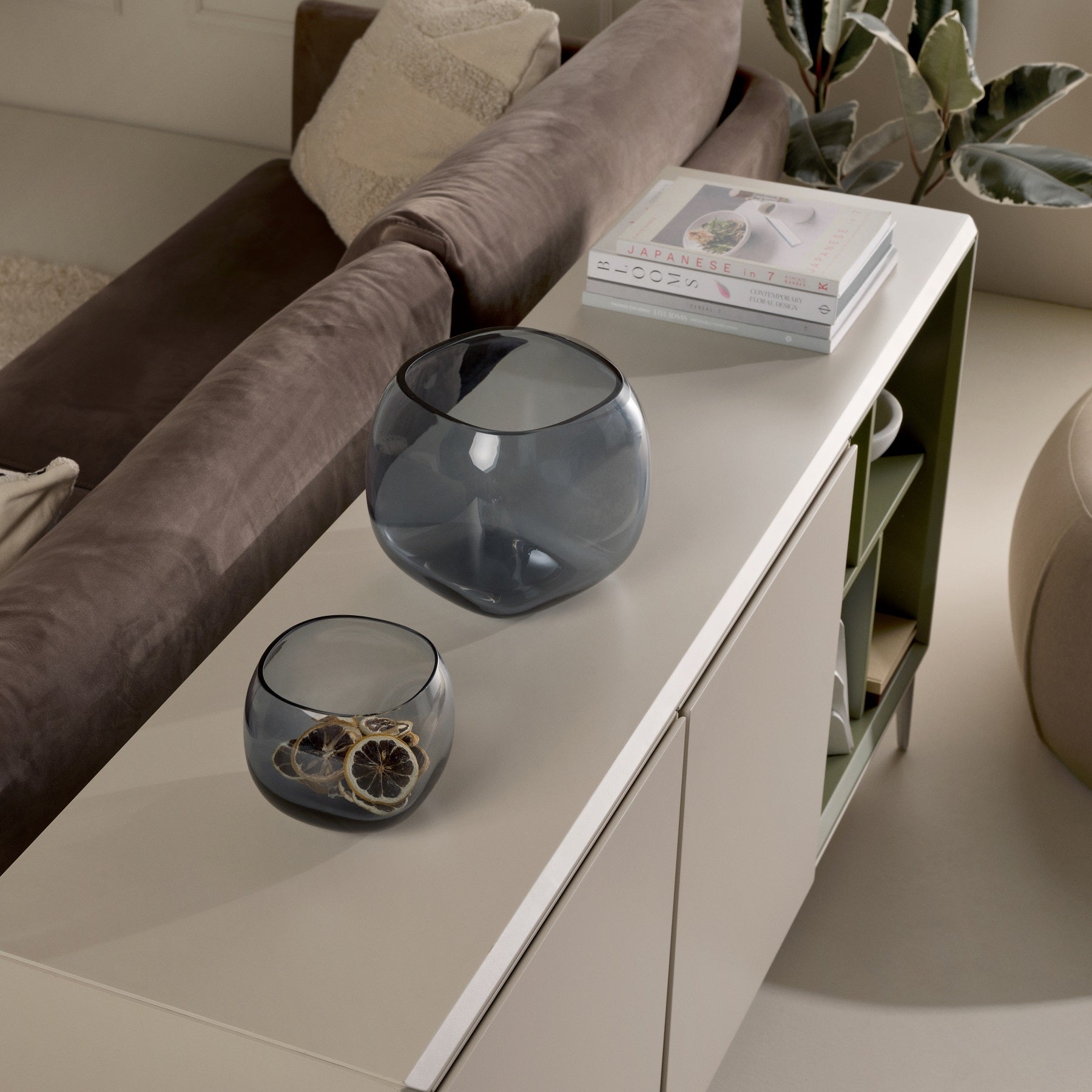 Two glass bowls on a light-colored cabinet with a couch and plant in the background