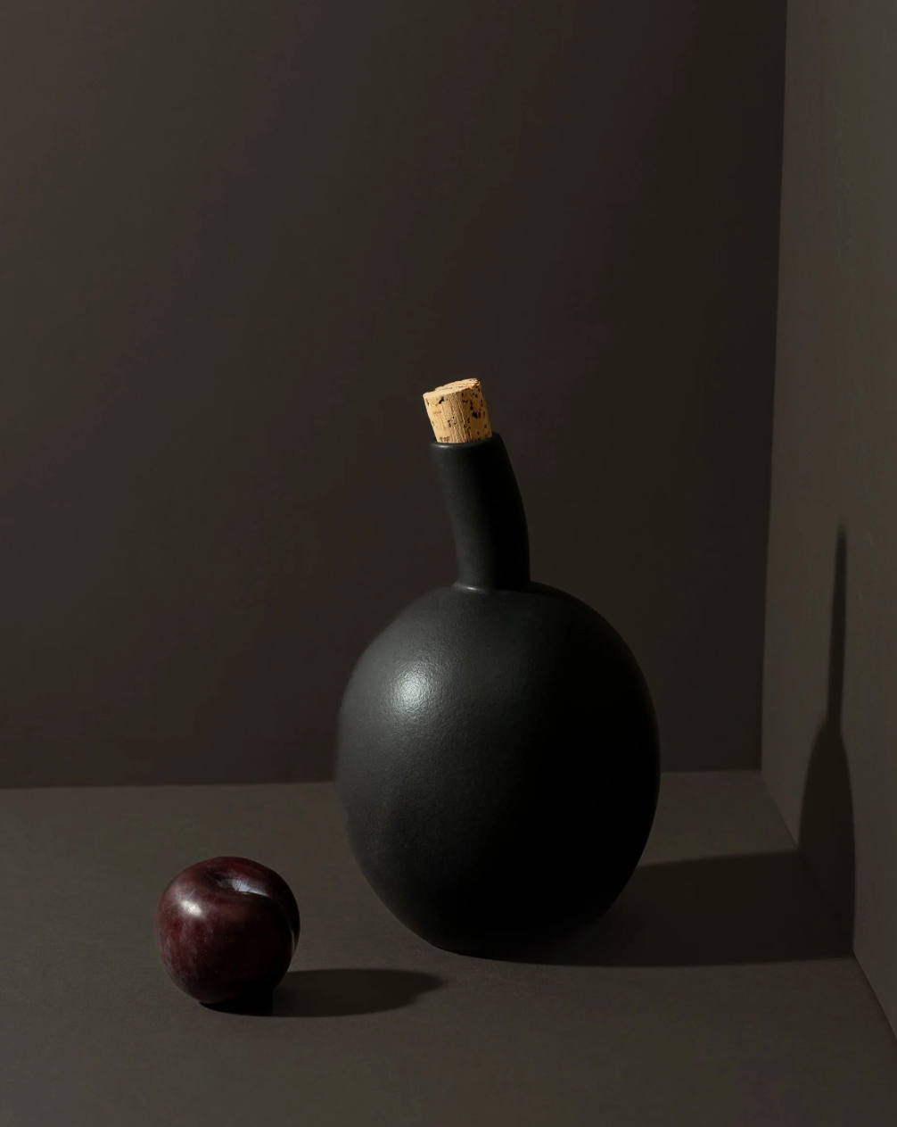 Dark bottle with cork stopper and plum on a dark background