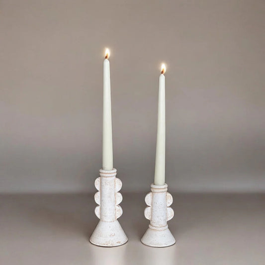 Two white candles in decorative candle holders on a neutral background