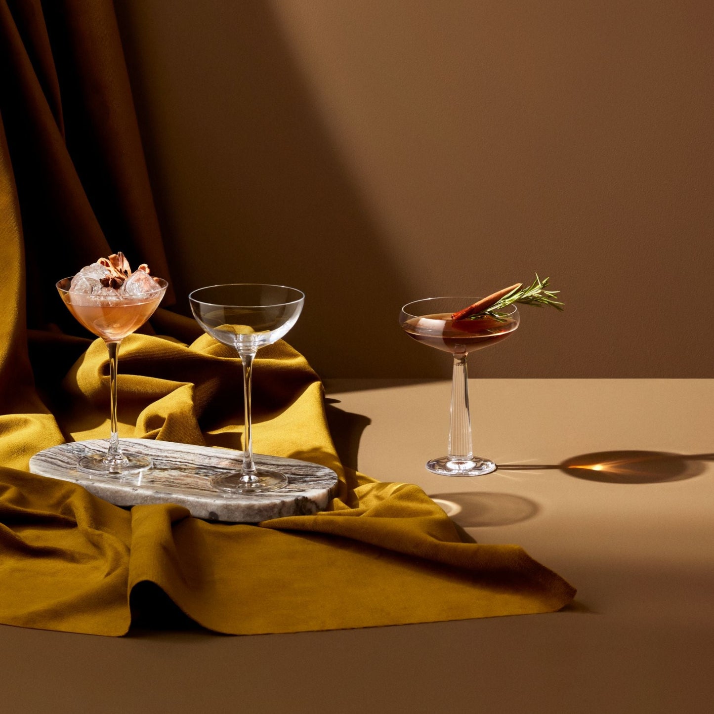 Three cocktail glasses with garnishes on a tray against a brown background
