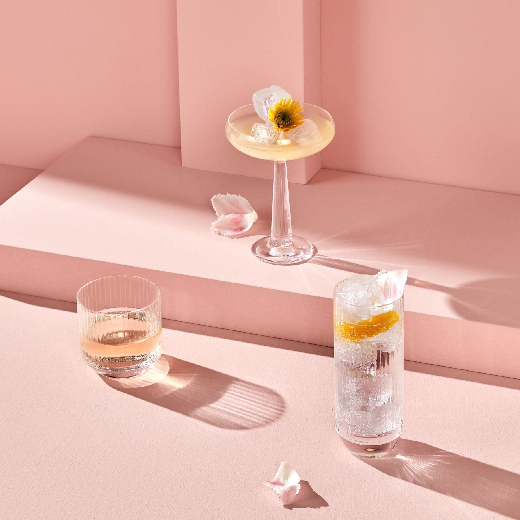 Three cocktails on a pink surface with a minimal background