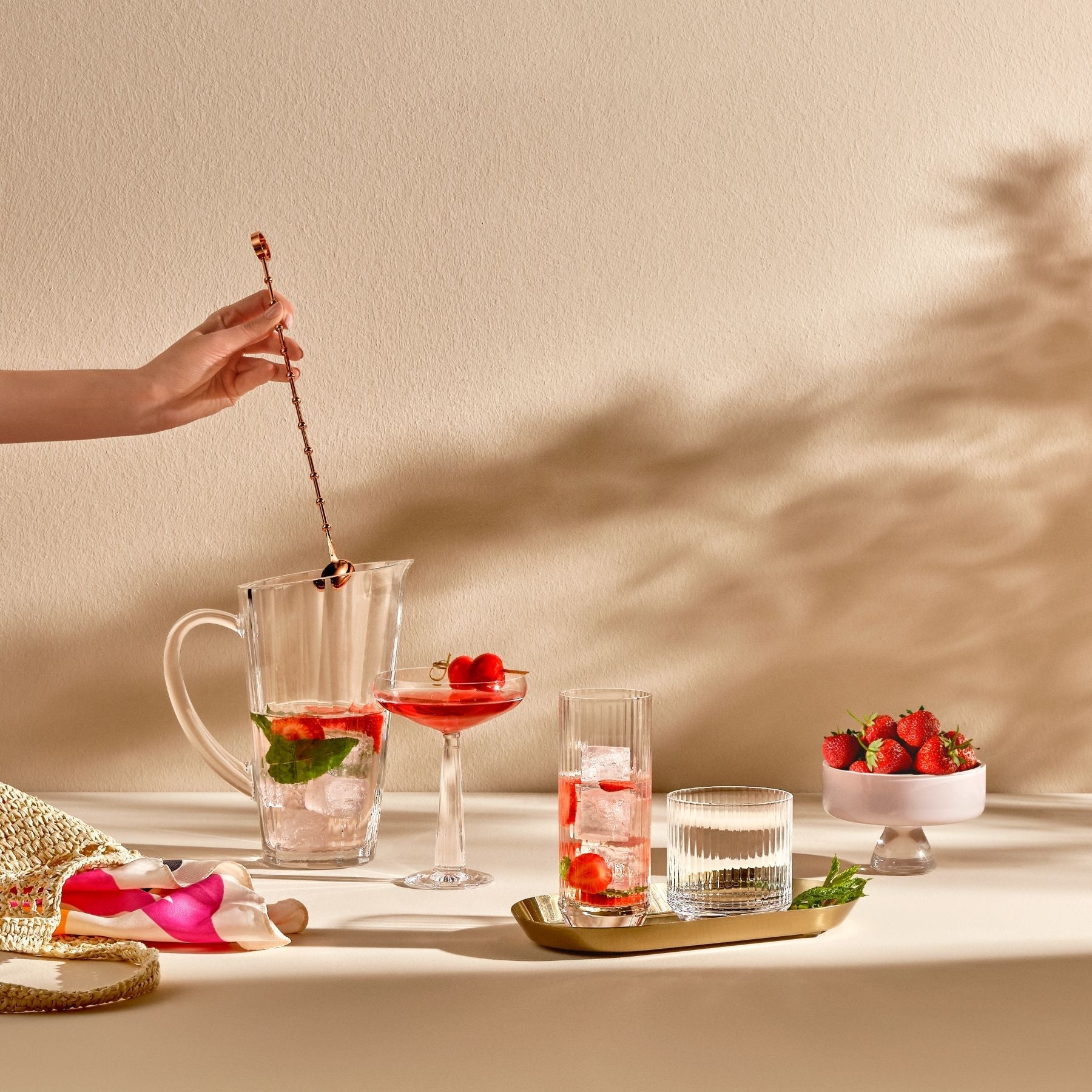 Cocktail preparation with a pitcher, glasses, and garnishes on a table.