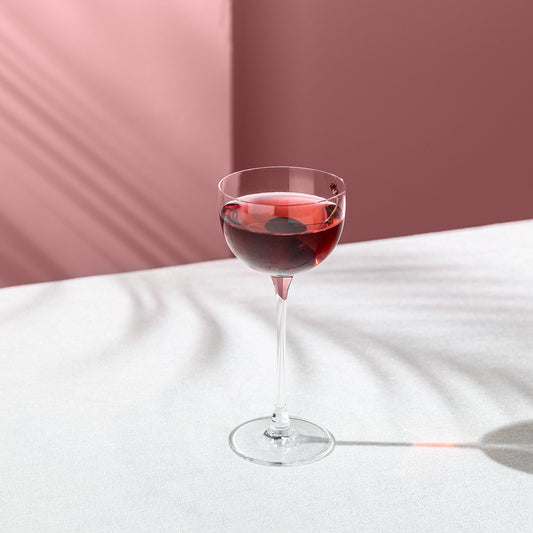 Wine glass with red wine on a white surface with a pink background