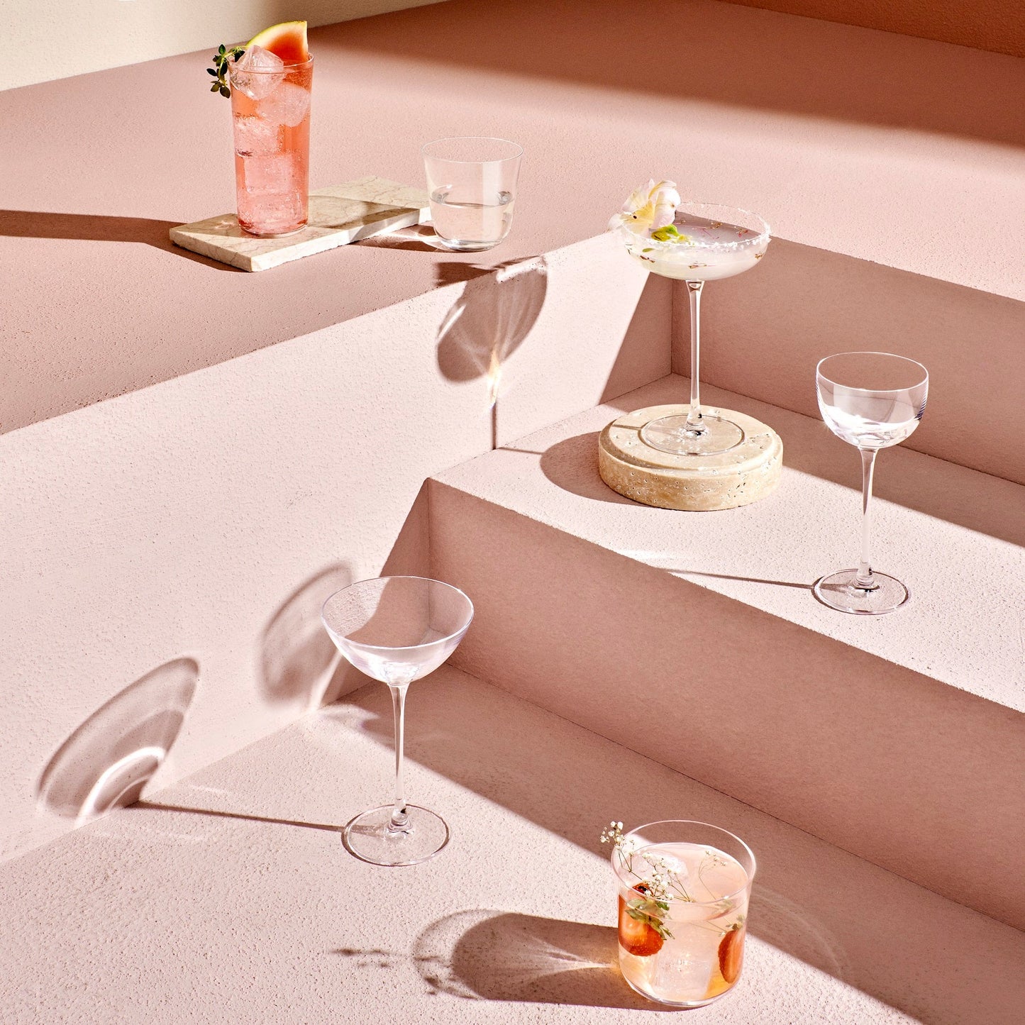 Cocktail glasses with drinks on a light pink surface