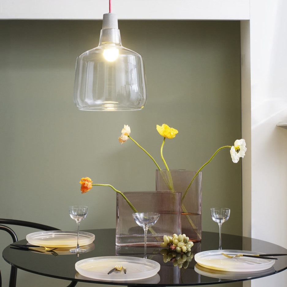Dining table setting with flowers, glasses, and plates under a pendant light.