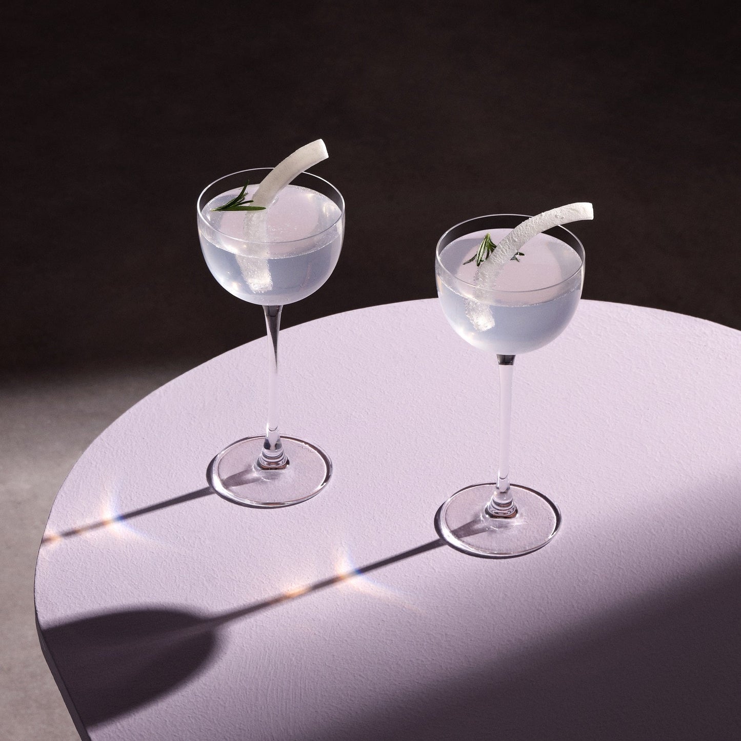 Two cocktails with garnishes on a round table against a dark background