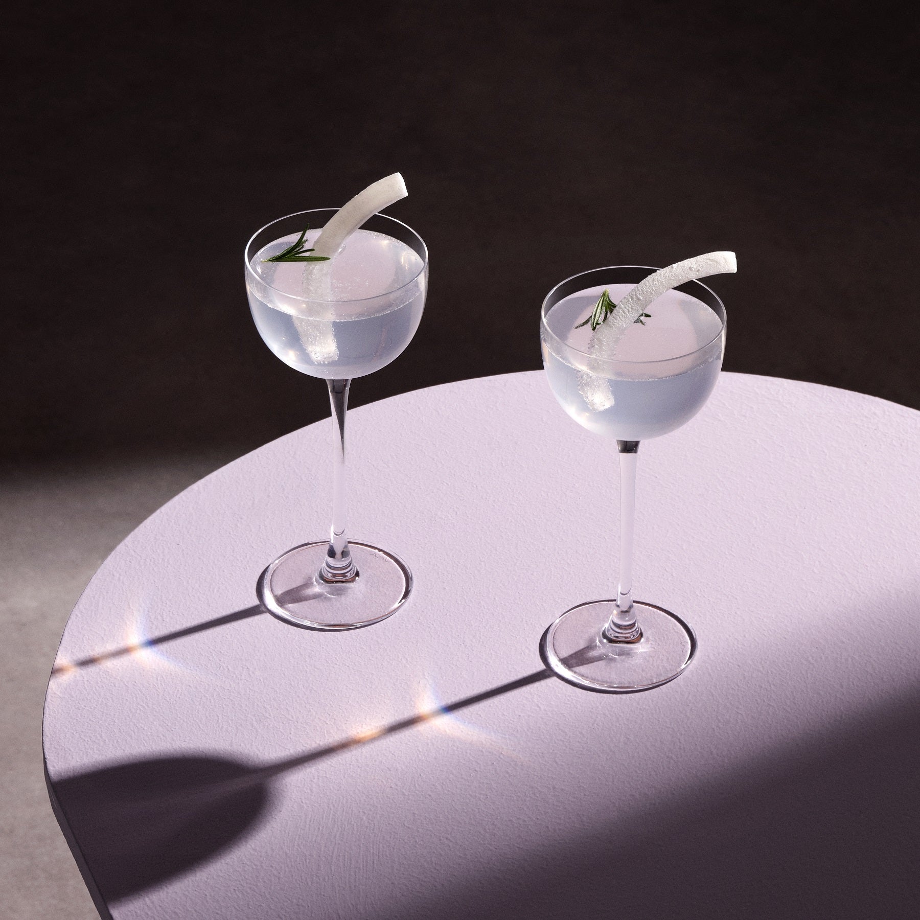 Two cocktails with garnishes on a round table against a dark background