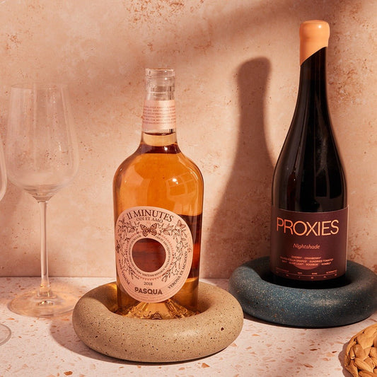 Two wine bottles, 'Basqua' and 'Proxies', on stone coasters with a glass in the background.