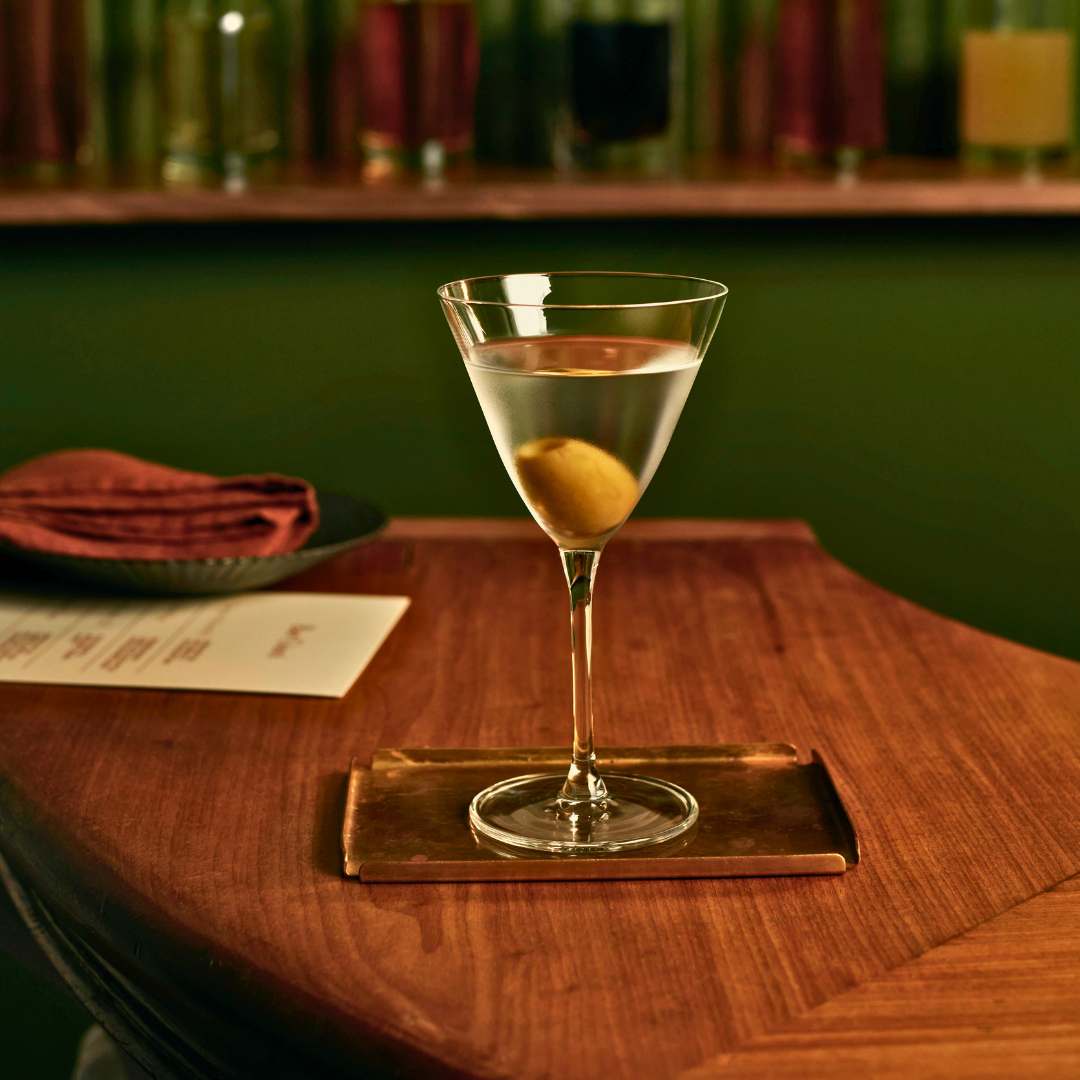 Cocktail glass with a lemon twist on a wooden bar counter with bottles in the background
