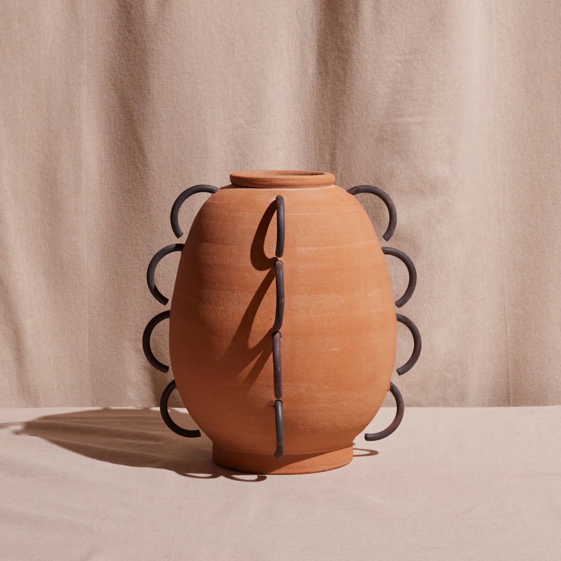 Terracotta vase with black metal accents on a beige background